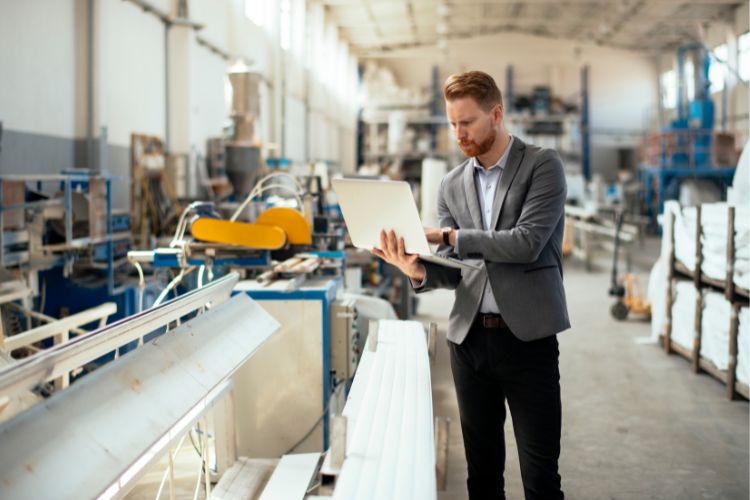 Man in a suit holding a laptop in a workshop